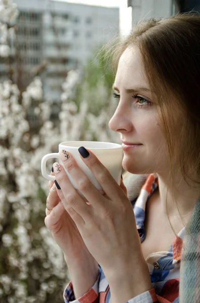 Молодая женщина с чашкой чая на балконе, цветущие деревья на заднем плане — стоковое фото