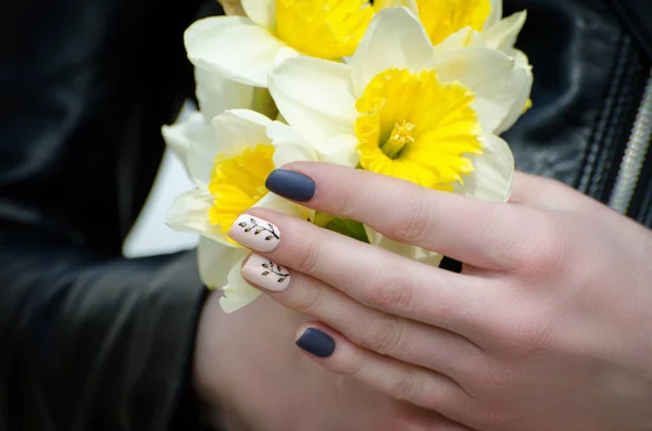 De handen van een jonge vrouw met narcissen, manicure. Close-up — Stockfoto