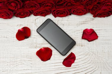 Smartphone, kırmızı gül ve yaprakları hafif ahşap zemin, üstten görünüm