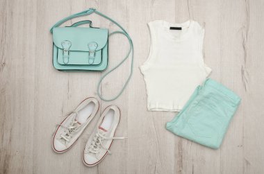 Beyaz bluz, nane renkli kot pantolon, beyaz spor ayakkabı ve çanta. Moda kavramı. Ahşap arka plan.