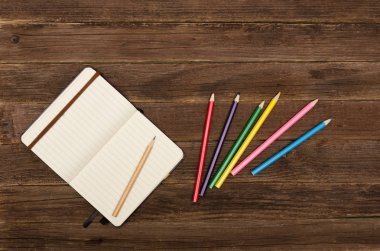 Not defteri ve ahşap bir masa üzerinde renkli kalemler