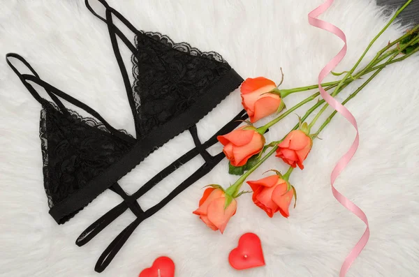 Black lace bra on white fur and a bouquet of orange roses. Fashionable concept. Top view — Stock Photo, Image