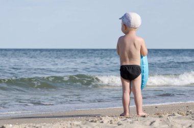 Çocuk yüzme şort bir yüzme daire ile deniz arka kıyısında duruyor