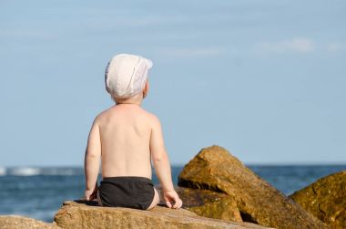 Küçük çocuk ile sırtını bir kayaya oturan deniz kıyısı, mavi gökyüzü, metin için yer