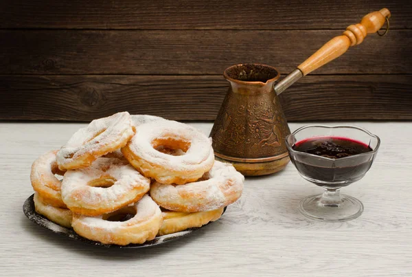Donuts em açúcar em pó, cezve de café e engarrafamento de passa de Corinto em um fundo de madeira — Fotografia de Stock