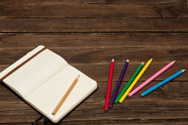 Not defteri ve ahşap bir masa üzerinde renkli kalemler