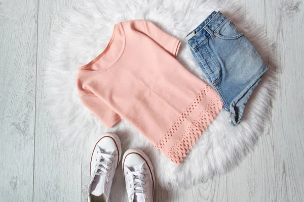 Pink blouse, denim shorts and sneakers on white fur, wooden background. Fashionable concept — Stock Photo, Image