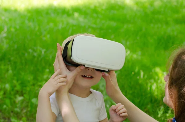 Мама виправляє його син окуляри віртуальної реальності на фоні зеленої трави — стокове фото