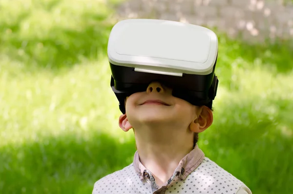 Niño en un casco de realidad virtual sobre un fondo de hierba verde —  Fotos de Stock