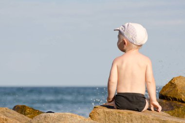 Küçük çocuk yüzme gövdeleri, mavi gökyüzü, metin için yer deniz kıyısına sırtında bir rock ile oturan