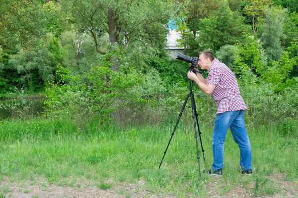 Photographer shooting from tripod against the background of river and green forest — Stock Photo, Image
