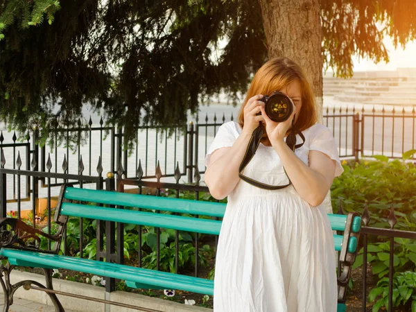 Dívka je pořizování snímků z fotoaparátu na pozadí lavička v parku — Stock fotografie