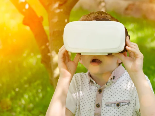 Niño en un casco de realidad virtual sobre un fondo de bosque verde. Tonificación —  Fotos de Stock