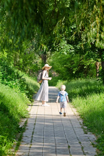 Anne ve oğlu yolun parkta yürüyorduk. Arkadan Görünüm. Dikey Çerçeve