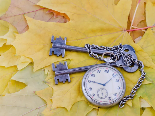 Clés anciennes et une montre de poche reposent sur des feuilles d'automne en érable jaune — Photo