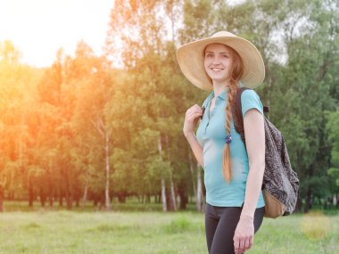 Sırt çantası ve şapka ile kız yaz orman karşı duruyor