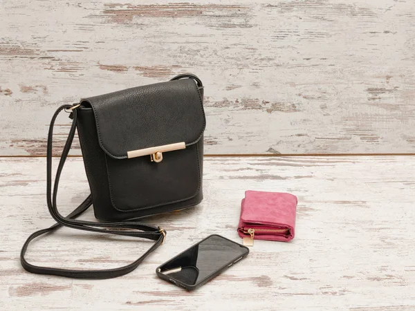 Malé černé ženské kabelku, peněženku a telefon na dřevěné pozadí. Módní pojem — Stock fotografie