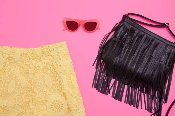 Parte de calções de renda amarelos, um saco preto com franja e óculos cor-de-rosa. Fundo rosa brilhante, close-up — Fotografia de Stock