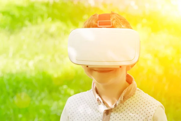 Niño en un casco de realidad virtual sonrisa sobre un fondo de hierba verde —  Fotos de Stock
