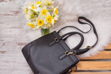 Siyah kadın çanta üzerinde beyaz kürk, nergis bir buket. Moda kavramı