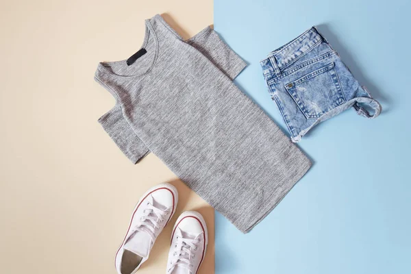 Modisches Konzept. Frauen im urbanen Stil. graues T-Shirt, weiße Turnschuhe und Jeans-Shorts auf weichem blauen Hintergrund — Stockfoto