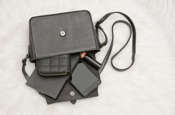 Открыть черную сумку с выброшенными вещами, записной книжкой, мобильным телефоном, сумочкой. Белый мех на заднем плане, вид сверху. концепция моды — стоковое фото