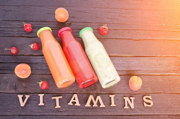 Three bottles with juice, fruit and inscription vitamins on a wooden background, food concept