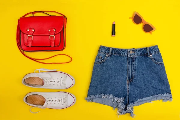 Calções de ganga, ténis brancos, bolsa vermelha. Fundo amarelo brilhante. Conceito na moda — Fotografia de Stock