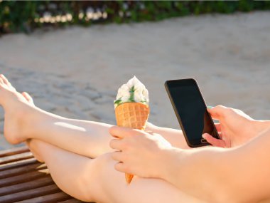 Smartphone ve dondurma eller, yan görünüm, yakın çekim. Yaz, şezlong