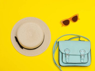Moda kavramı. Kadın hasır şapka, nane çanta, güneş gözlüğü. Sarı arka plan, üstten görünüm
