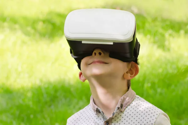 Niño en un casco de realidad virtual sobre un fondo de hierba verde —  Fotos de Stock