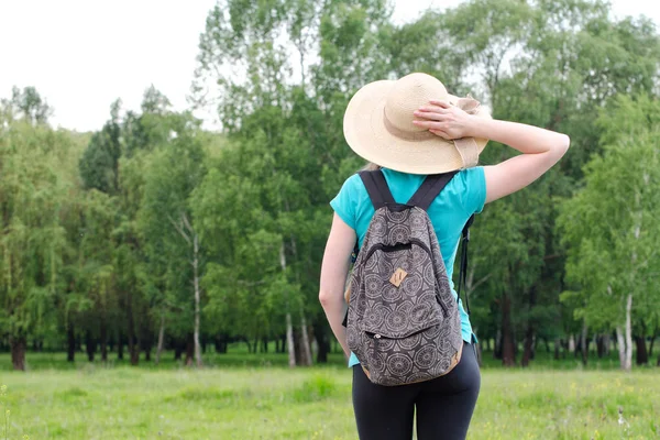 Chica en sombrero y mochila sostiene la mano detrás de la cabeza sobre un fondo de bosque verde — Foto de Stock