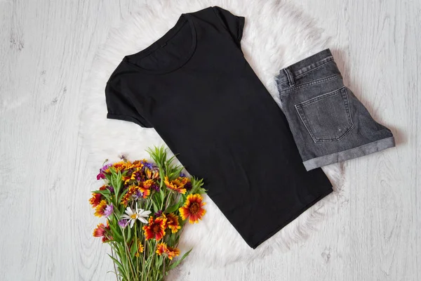 Siyah top, kot şort ve beyaz kürk, ahşap arka plan üzerinde kır çiçekleri buketi. Moda kavramı