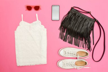 Beyaz dantel üst, siyah çanta, beyaz spor ayakkabı, gözlük ve telefon. Parlak pembe arka plan. Moda kavramı