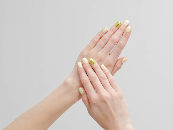 Beautiful female hands with a manicure on a light background. Yellow with gold nails