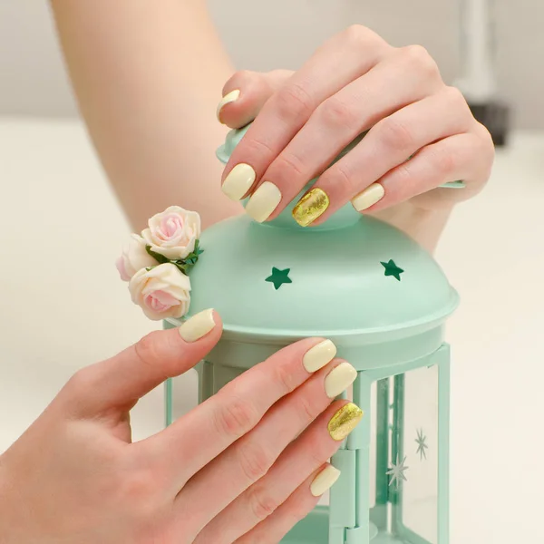 Belle mani femminili con una manicure e un candelabro su uno sfondo leggero. Giallo con chiodi in oro — Foto Stock