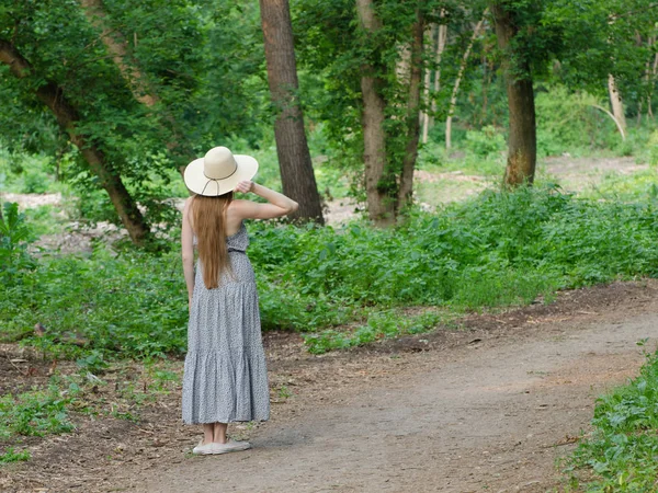 Hermosa chica en un sombrero y el pelo largo está de pie en un sendero en un bosque verde — Foto de Stock