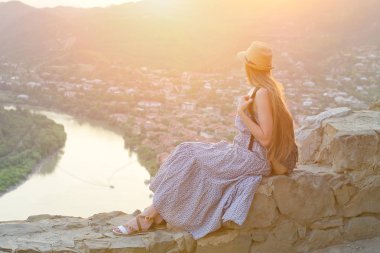 Sırt çantası ve oturma ve nehir, dağ ve şehir görünümünü hayran şapka ile güzel kız