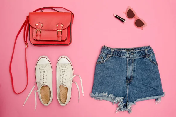 Kot şort, beyaz spor ayakkabı, kırmızı çanta. Parlak pembe arka plan. Moda kavramı