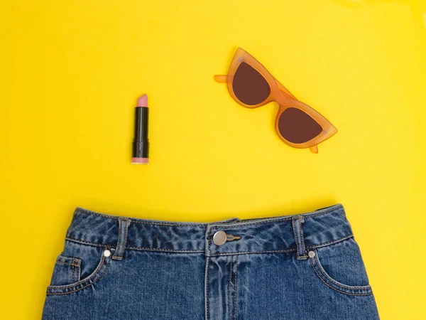 Kot şort, güneş gözlüğü ve ruj. Parlak sarı arka plan. Moda kavramı