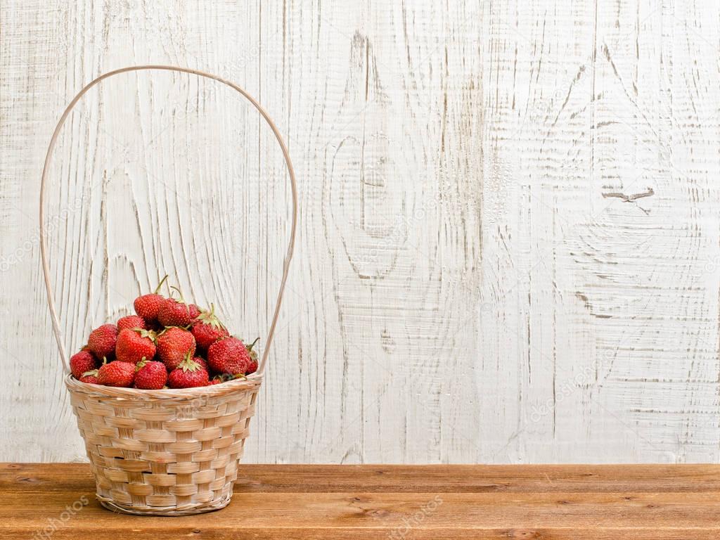 Wicker basket of ripe strawberries standing on a brown table on white wooden background