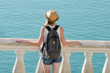 Kız şapka ve bir sırt çantası denizin üzerinde duruyor. Arkadan görüntülemek