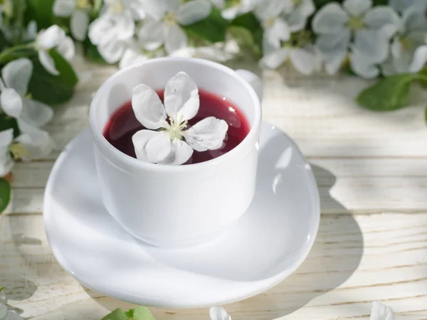 Weißer Becher Tee auf einem Holztisch, im Hintergrund blühen Apfelblüten. sonnig, Seitenblick — Stockfoto
