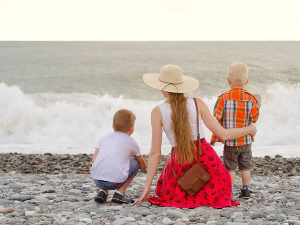 Anne ve sahilde oturan ve dalgaları seyretmekten iki oğlu. Arkadan görüntülemek