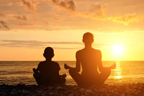 Anya és fia a strandon, a lótusz helyzet meditálni. Sziluettek, naplemente — Stock Fotó