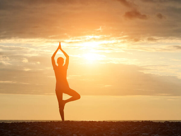 Girl at sunset practicing yoga at the seashore, silhouette
