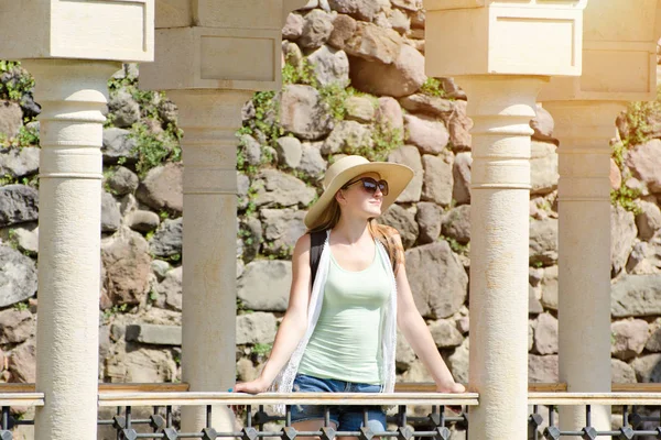 Menina em um chapéu e óculos escuros que estão entre colunas. Dia ensolarado — Fotografia de Stock