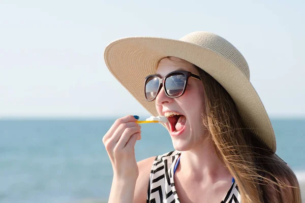 Дівчина в капелюсі їсть ложку морозива. Море на фоні. Сонячний день — стокове фото