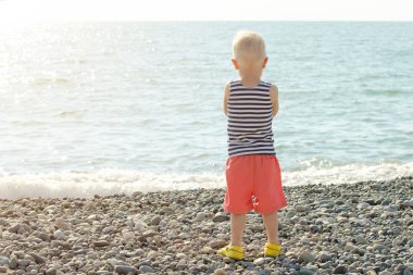 Boy Çizgili tişört içinde sahilde duran ve denize bakarak. Arkadan Görünüm