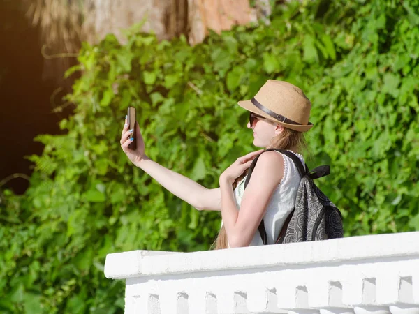 Girl in a hat and with a backpack makes selfie in the park — Stock Photo, Image
